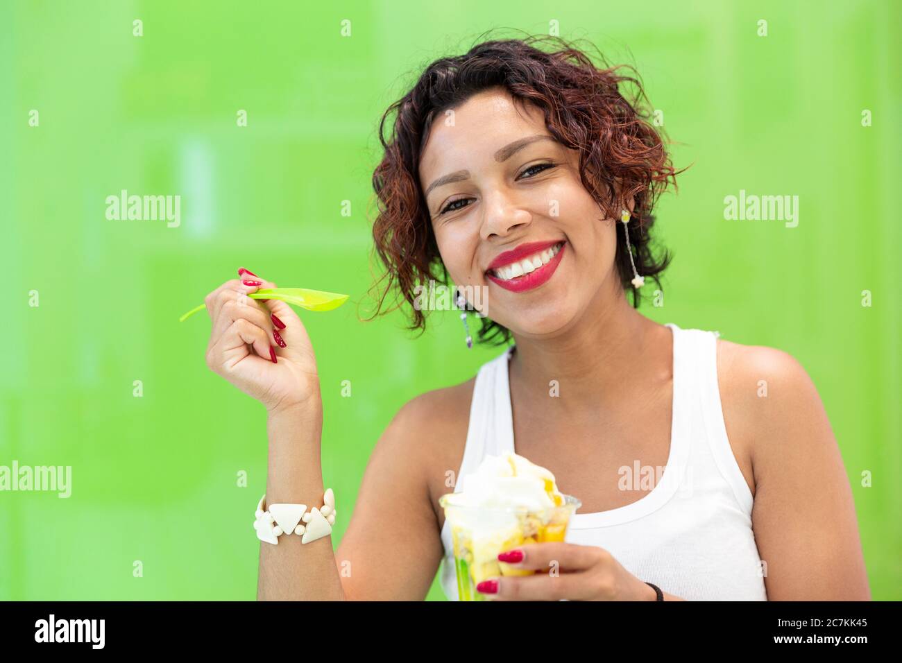 Primo piano di una donna latina sorridente che tiene un gelato su sfondo verde. Spazio per il testo. Messa a fuoco selettiva. Concetto di estate e stile di vita. Foto Stock
