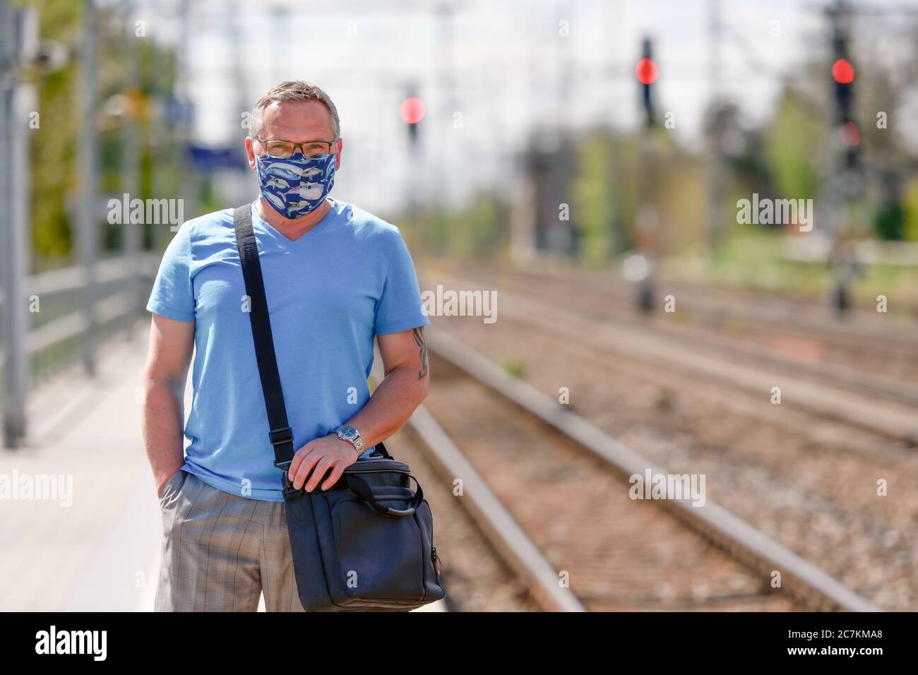 Uomo con guardia bocca aspetta il treno alla stazione, guardando la macchina fotografica, tracce in background Foto Stock