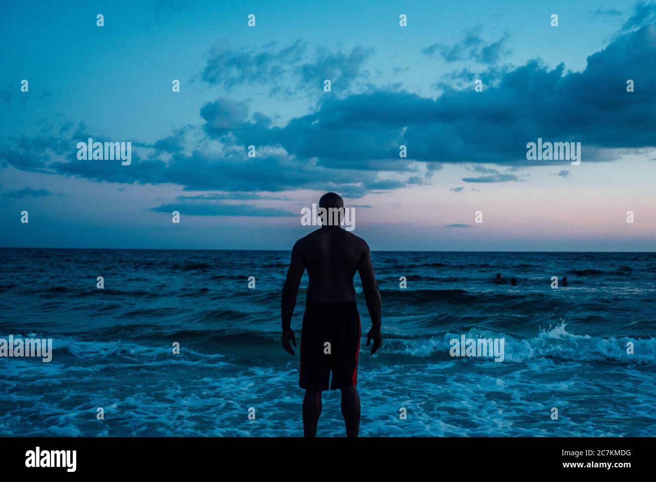 Uomo afroamericano in piedi vicino al mare sotto un blu cielo nuvoloso girato da dietro Foto Stock