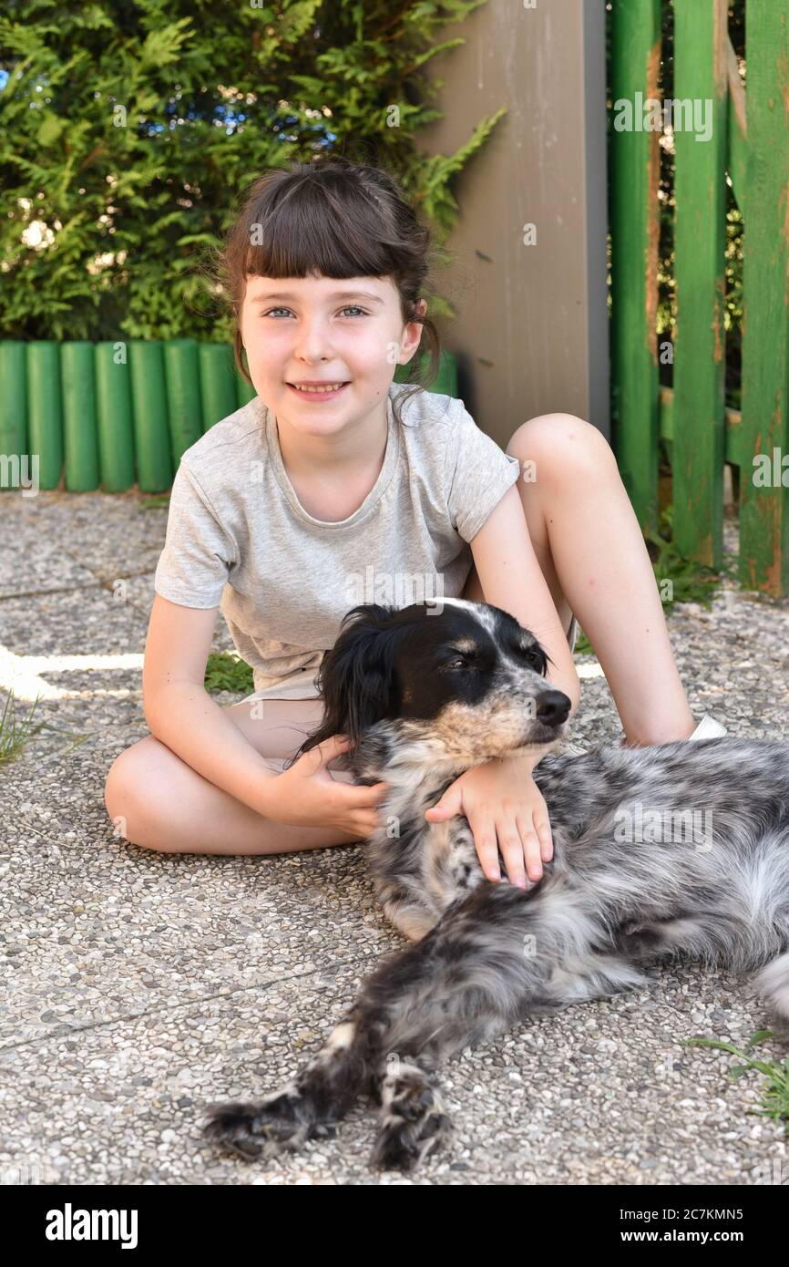 Una bambina si siede all'aperto accanto al suo cane, ritratto impostato all'aperto con un animale domestico Foto Stock