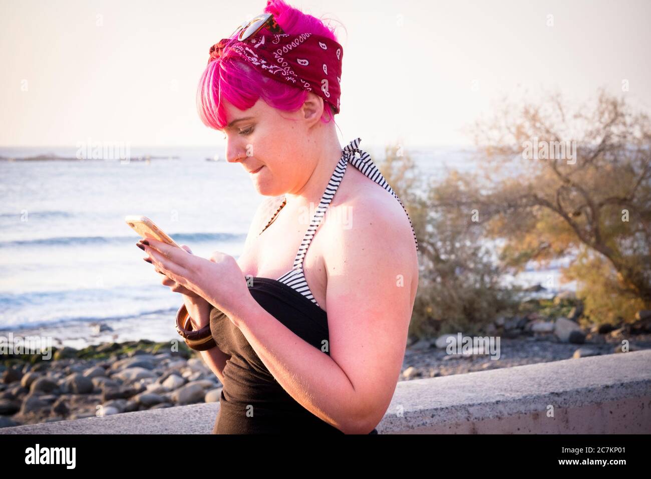 Persone alternative con capelli rosa e moderno telefono cellulare collegato - giovane donna e divsity lifestyle concetto - vista oceano e attività turistica Foto Stock