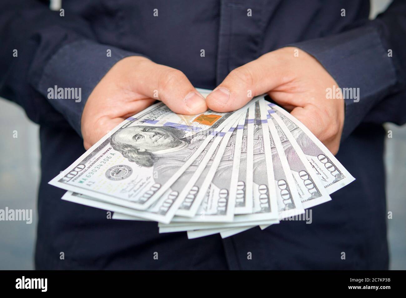Mani maschili con orologio da polso è considerato dollari americani. Mani che tengono contanti del dollaro. 1000 dollari in 100 fatture in un primo piano della mano dell'uomo su un buio Foto Stock