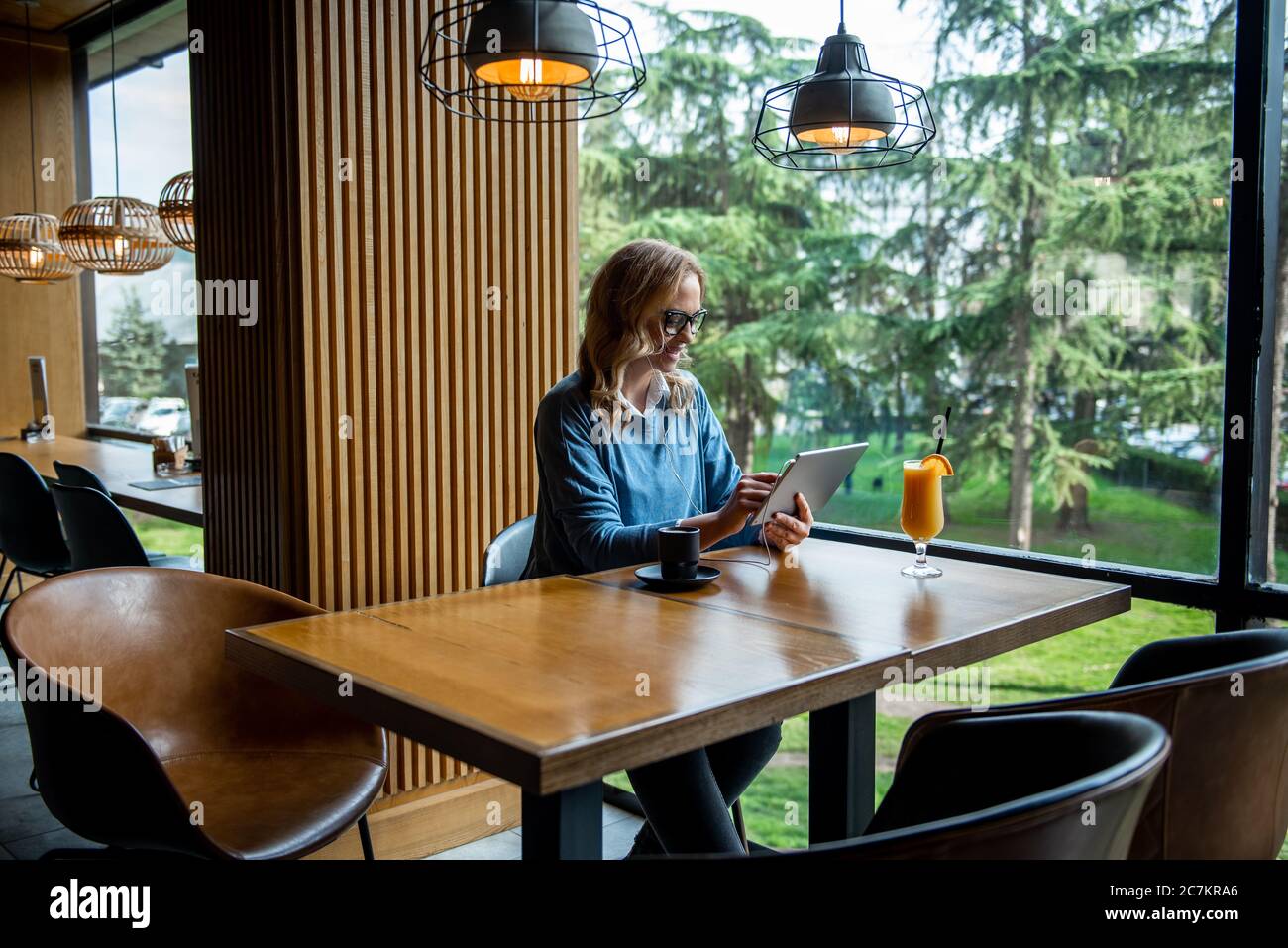 Sorridente donna d'affari che ascolta musica e utilizza tablet in un concetto di caffetteria, stile di vita e business Foto Stock