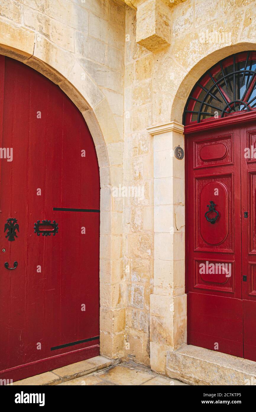 Scatto verticale di porte in legno rosso con maniglie in metallo nero di un vecchio edificio fatto di mattoni Foto Stock