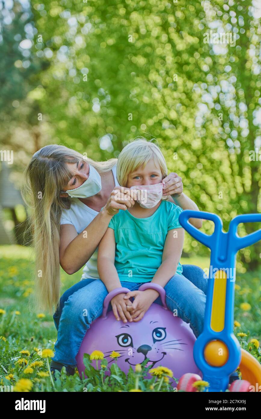 Madre mette su maschera facciale, figlia, parco giochi, crisi corona, Ratisbona, Baviera, Germania Foto Stock