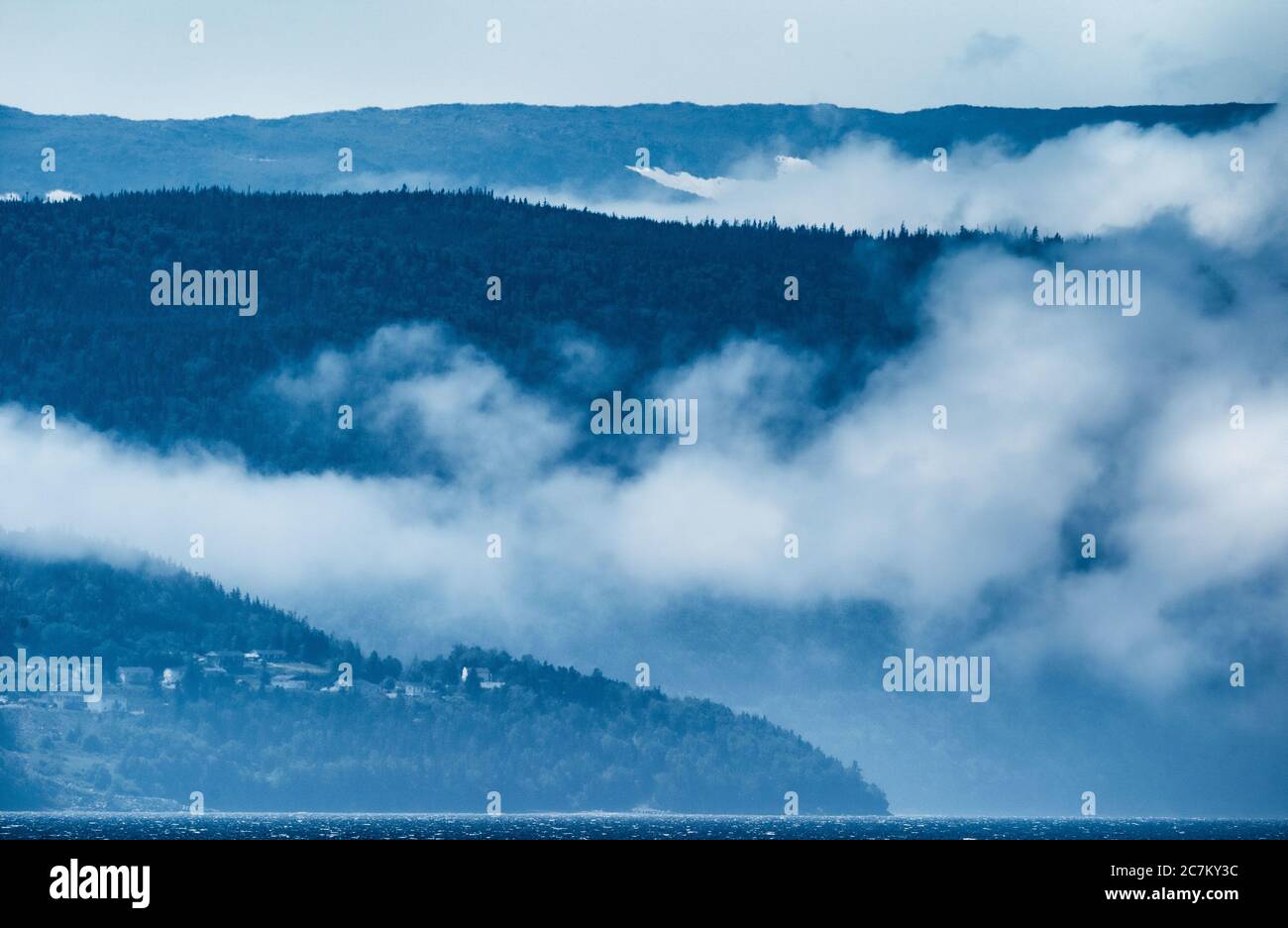 Ampio scatto di una catena montuosa con nebbia e un piccola città sotto in una giornata fredda Foto Stock