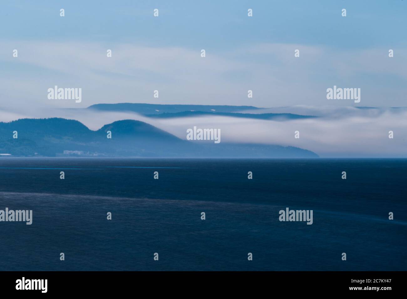 Bellissimo scatto di un oceano blu profondo e di una montagna raggio d'azione con nebbia in una giornata buia Foto Stock