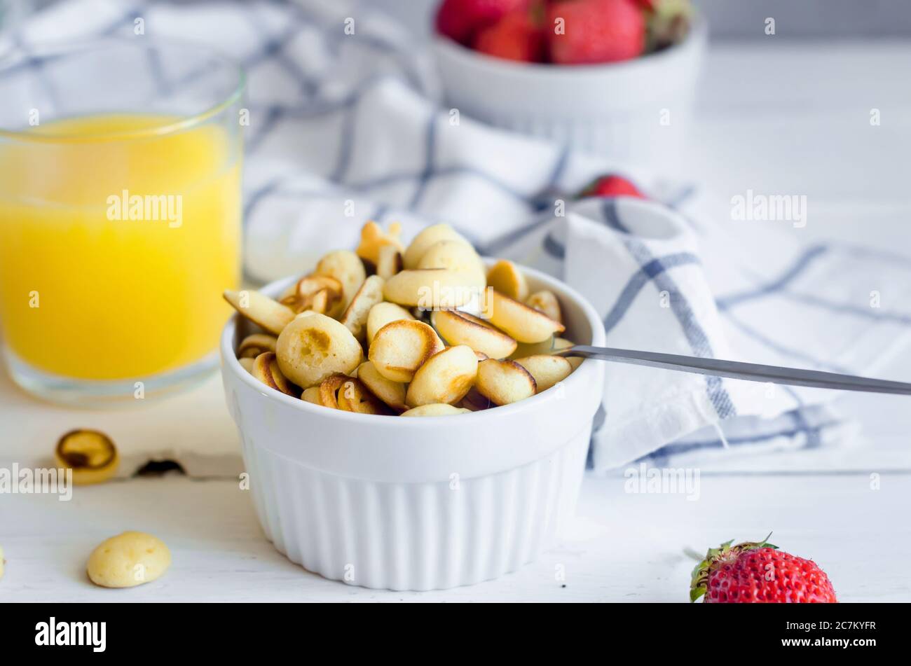 Ciotola bianca con minuscola frittella con fragole e bicchiere di succo d'arancia. Cucina alla moda, spazio copia. Mini pancake nuovo concetto di tendenza alimentare. Foto Stock