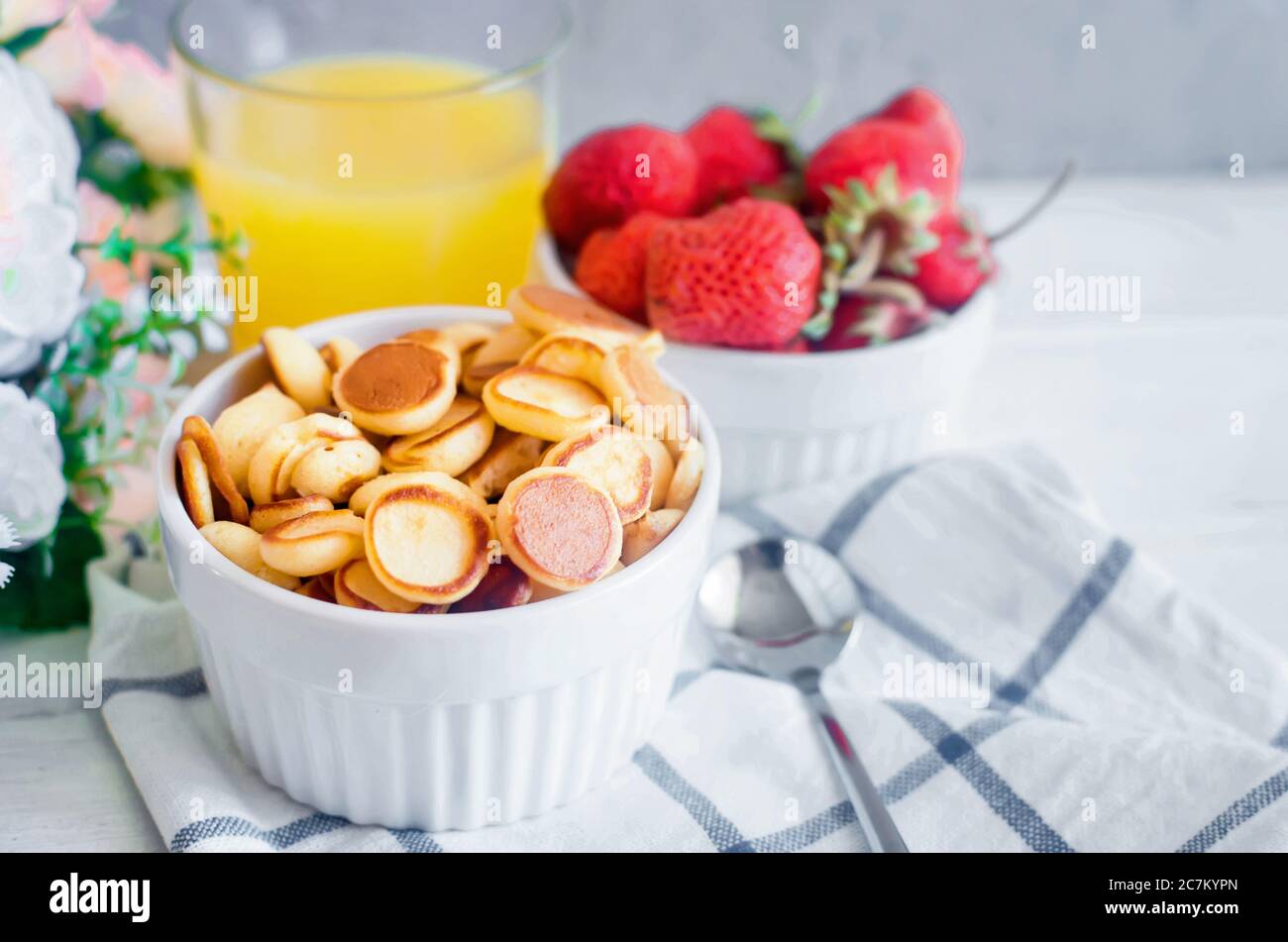Ciotola bianca con minuscola frittella con fragole e bicchiere di succo d'arancia. Cucina alla moda, spazio copia. Mini pancake nuovo concetto di tendenza alimentare. Foto Stock