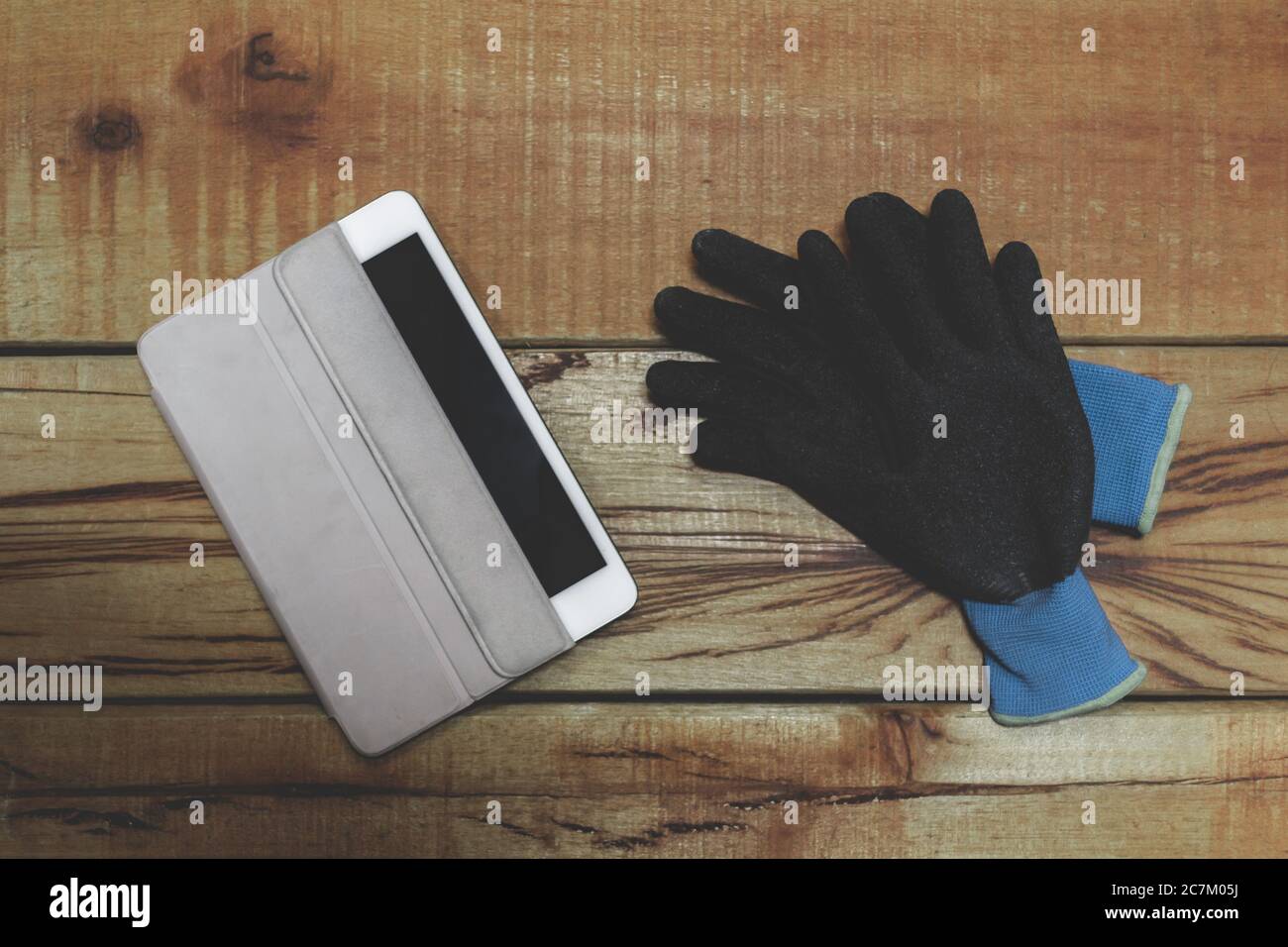 Un paio di guanti da lavoro e una compressa vuota parzialmente scoperta su un banco di lavoro in legno Foto Stock