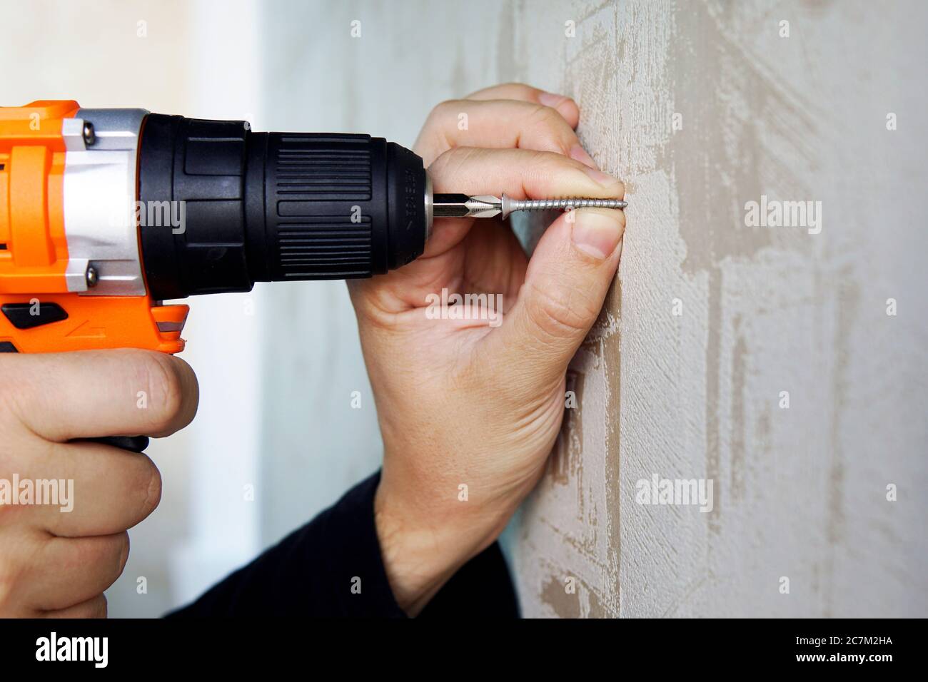 Avvitando una vite nella parete con un cacciavite elettrico da vicino. Riparazione in appartamento o casa. Foto Stock