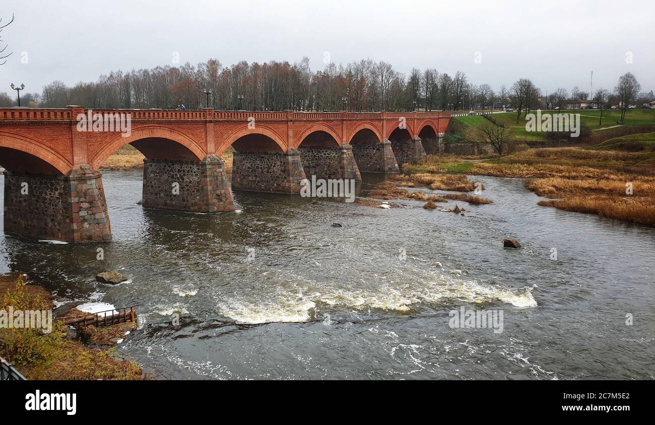 Vecchio ponte di mattoni del fiume Venta in Kuldiga Lettonia con un cielo cupo Foto Stock