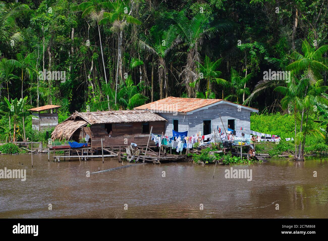 Case su palafitte sulle rive del fiume Amazzonia con linea di lavaggio all'esterno che asciuga la lavanderia del proprietario, e la foresta pluviale oltre Foto Stock