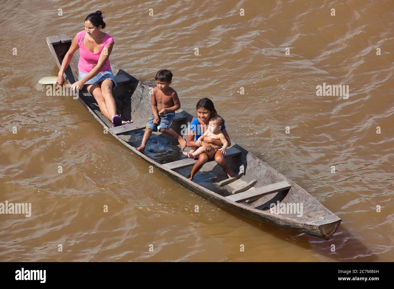 Una madre e i suoi tre figli, uno un bambino in una canoa in legno sul fiume Amazzonia Foto Stock