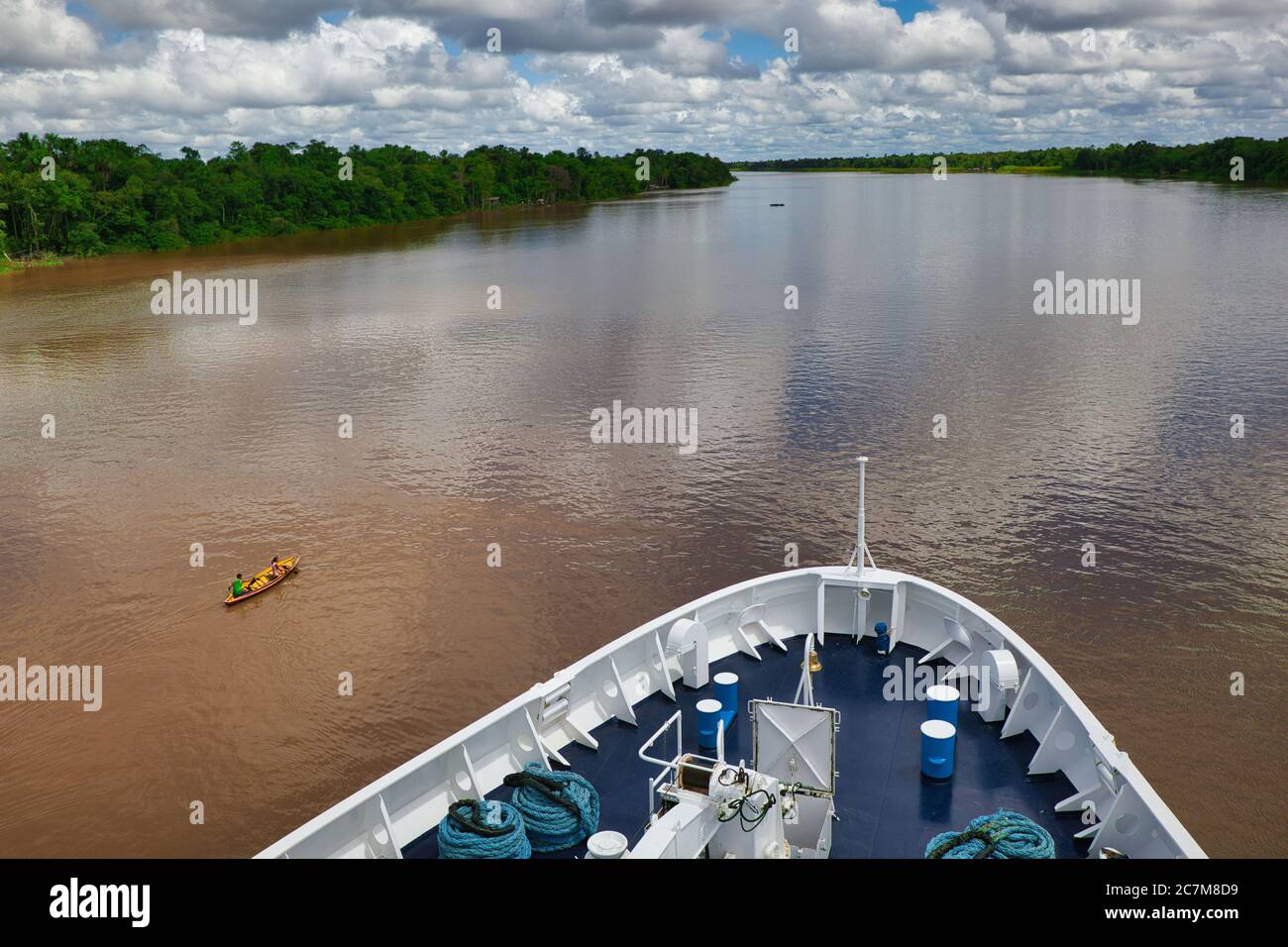 Dalle incuci di una grande nave, una vista del fiume Amazzonia davanti con alberi e foreste da un lato e la gente in una canoa di legno aperta che passa Foto Stock
