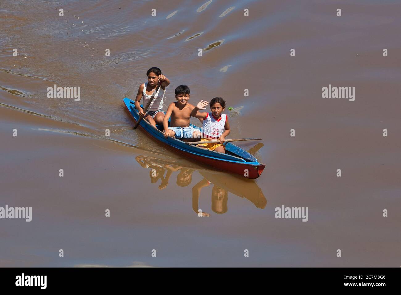 Tre bambini, bambina di fronte che sventolano alla macchina fotografica, in canoa sul fiume Amazon vicino a Belem, nello stato di Para, Brasile. Foto Stock