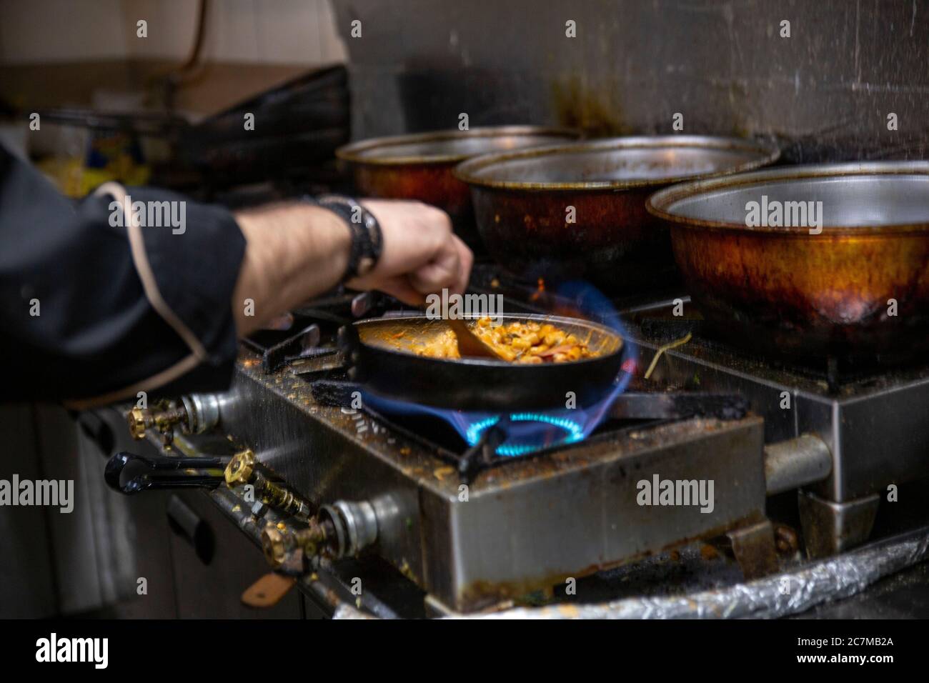 Fuoco selettivo di un cuoco che cucinano il cibo delizioso sopra la padella Foto Stock