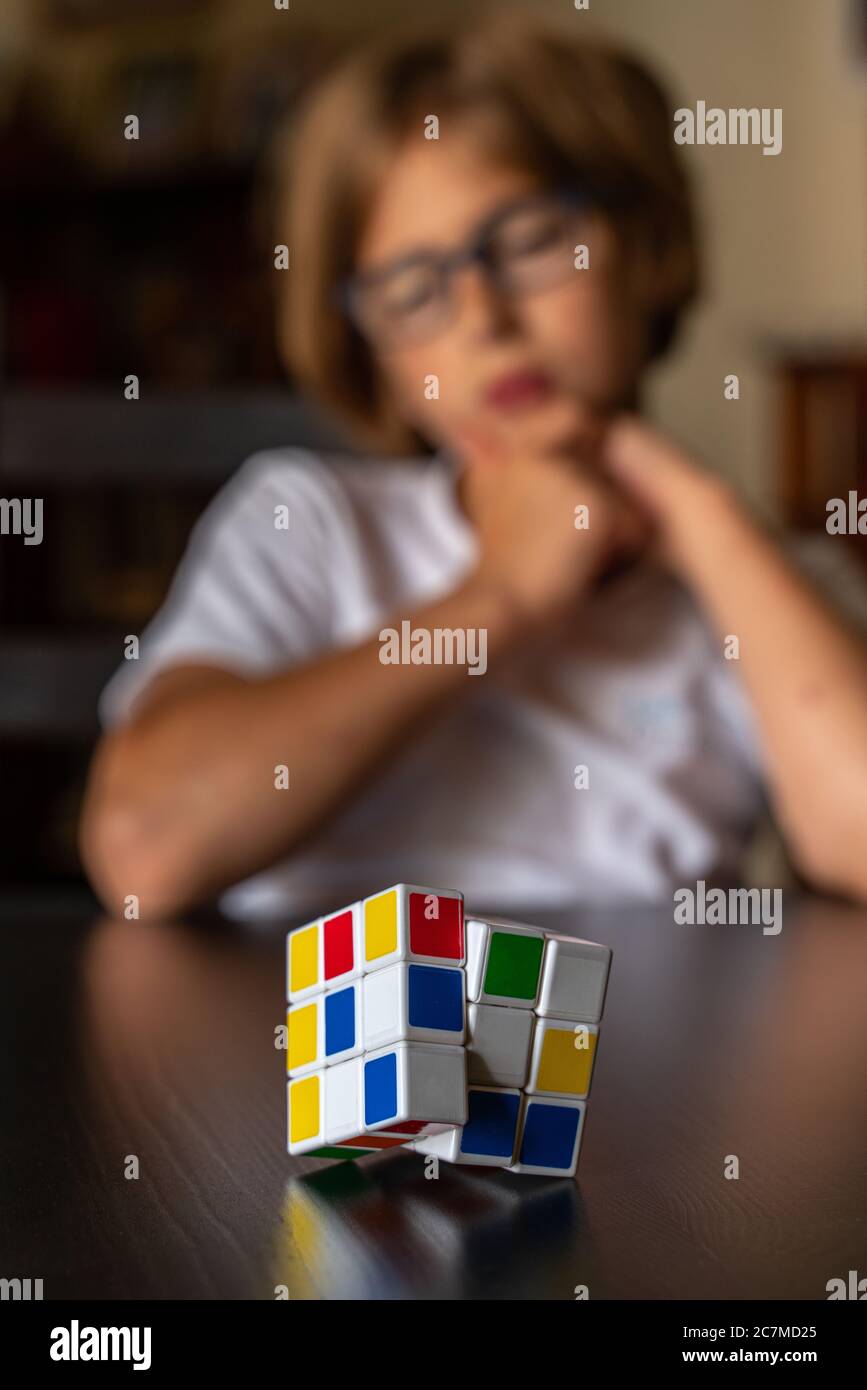Bambino con gli occhiali pensa come risolvere il cubo di Rubik Foto Stock