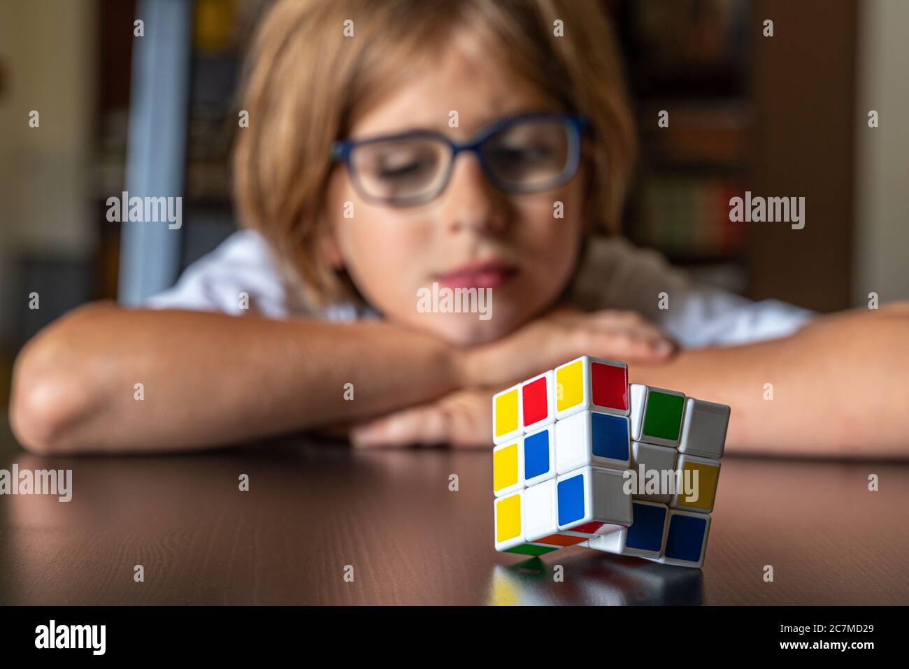 Bambino con gli occhiali pensa come risolvere il cubo di Rubik Foto Stock