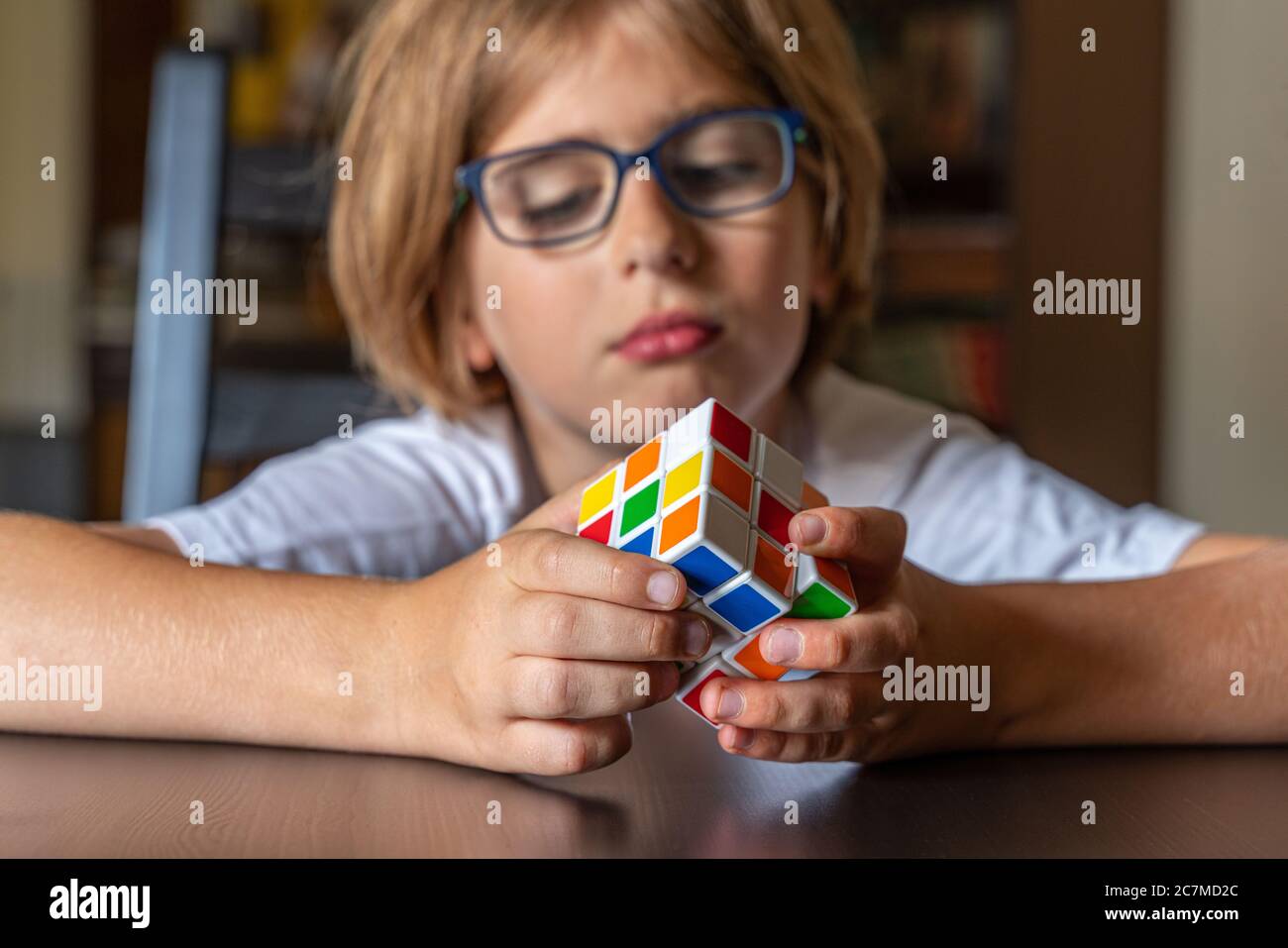 Bambino con i bicchieri cercando di risolvere il cubo di Rubik Foto Stock