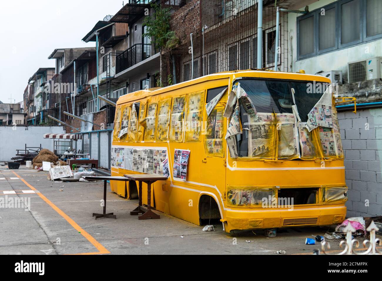 Un autobus giallo senza pneumatici e in rovina un parcheggio con giornali a lato Foto Stock