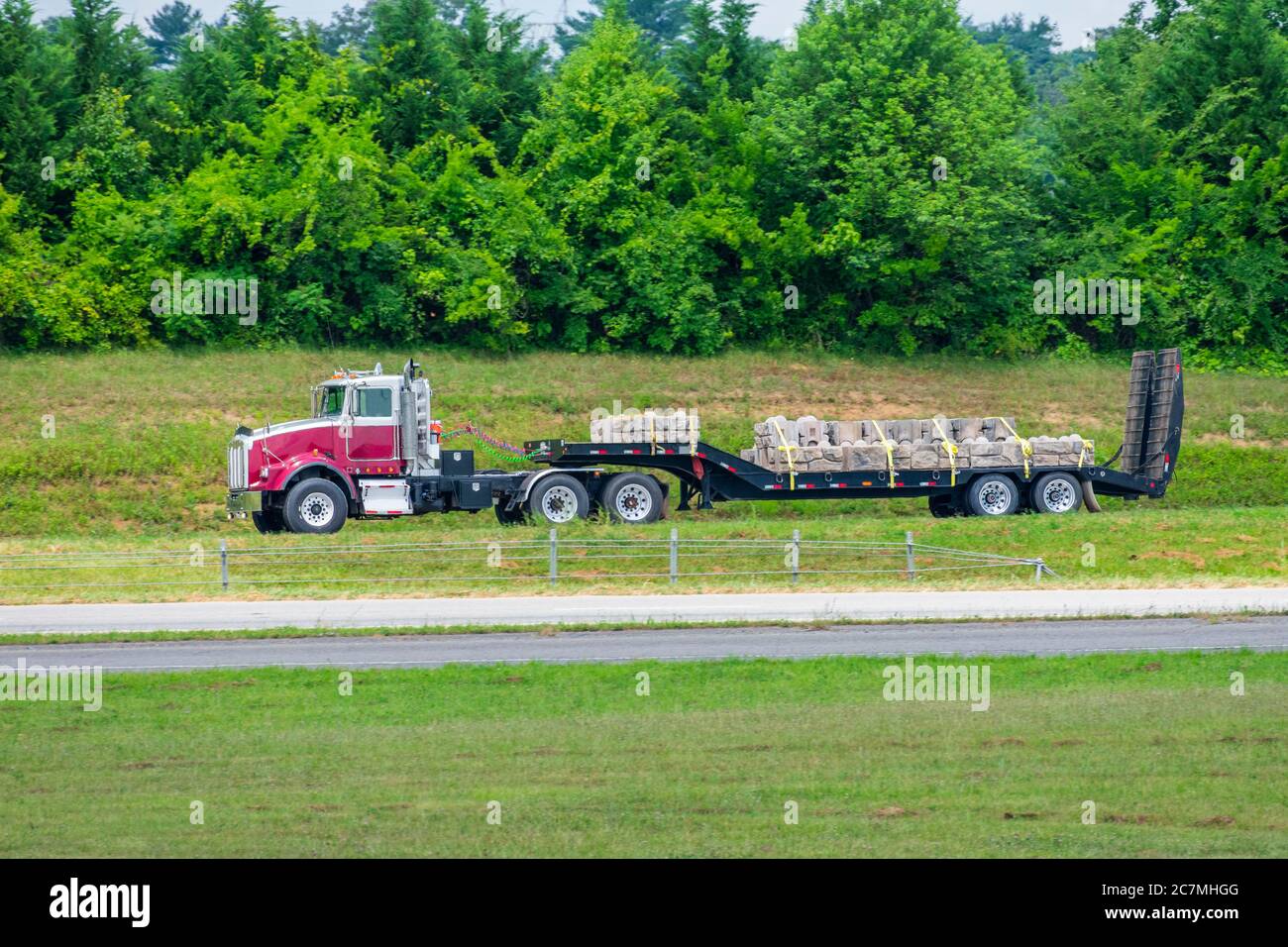 Immagine laterale orizzontale di un carro a 18 ruote con pianale che scende lungo l'autostrada trasportando un carico di pietra per la costruzione. Foto Stock
