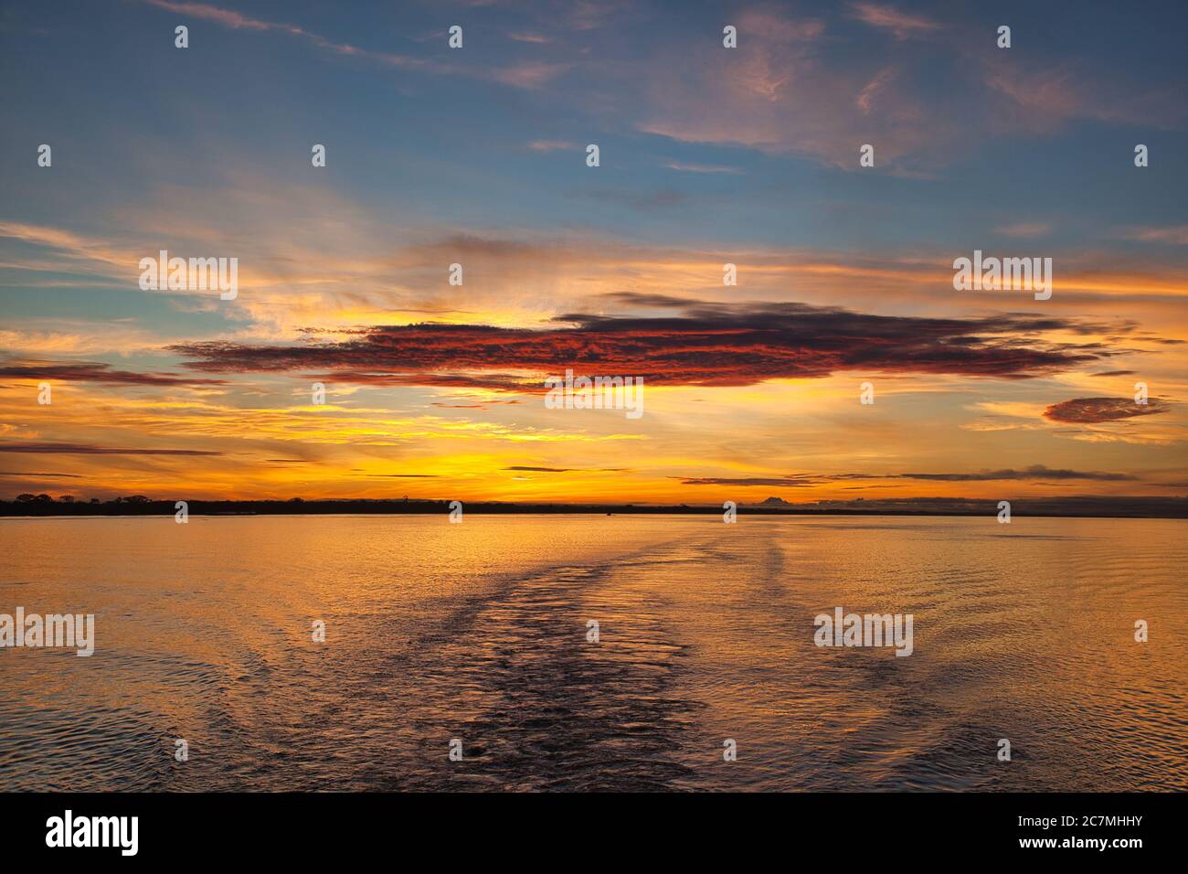 Alba sul Rio delle Amazzoni alle 6:00 con spettacolare arancione rosso e giallo mattina alba cielo e la scia della nave in primo piano Foto Stock