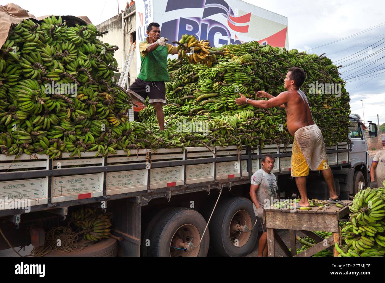 L'uomo lancia un grosso grappolo di banane fino a un altro uomo che le carica sul posto su un camion, al mercato di Manaus, Stato amazzonico, Brasile Foto Stock