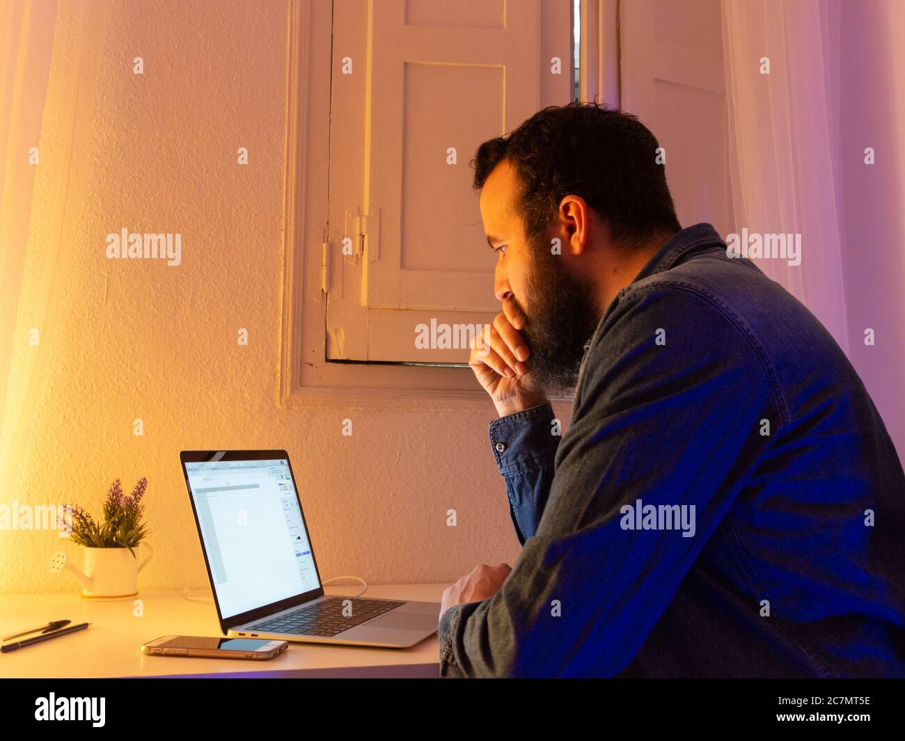 Uomo sopportato seduto e guardando qualcosa sul suo laptop Foto Stock