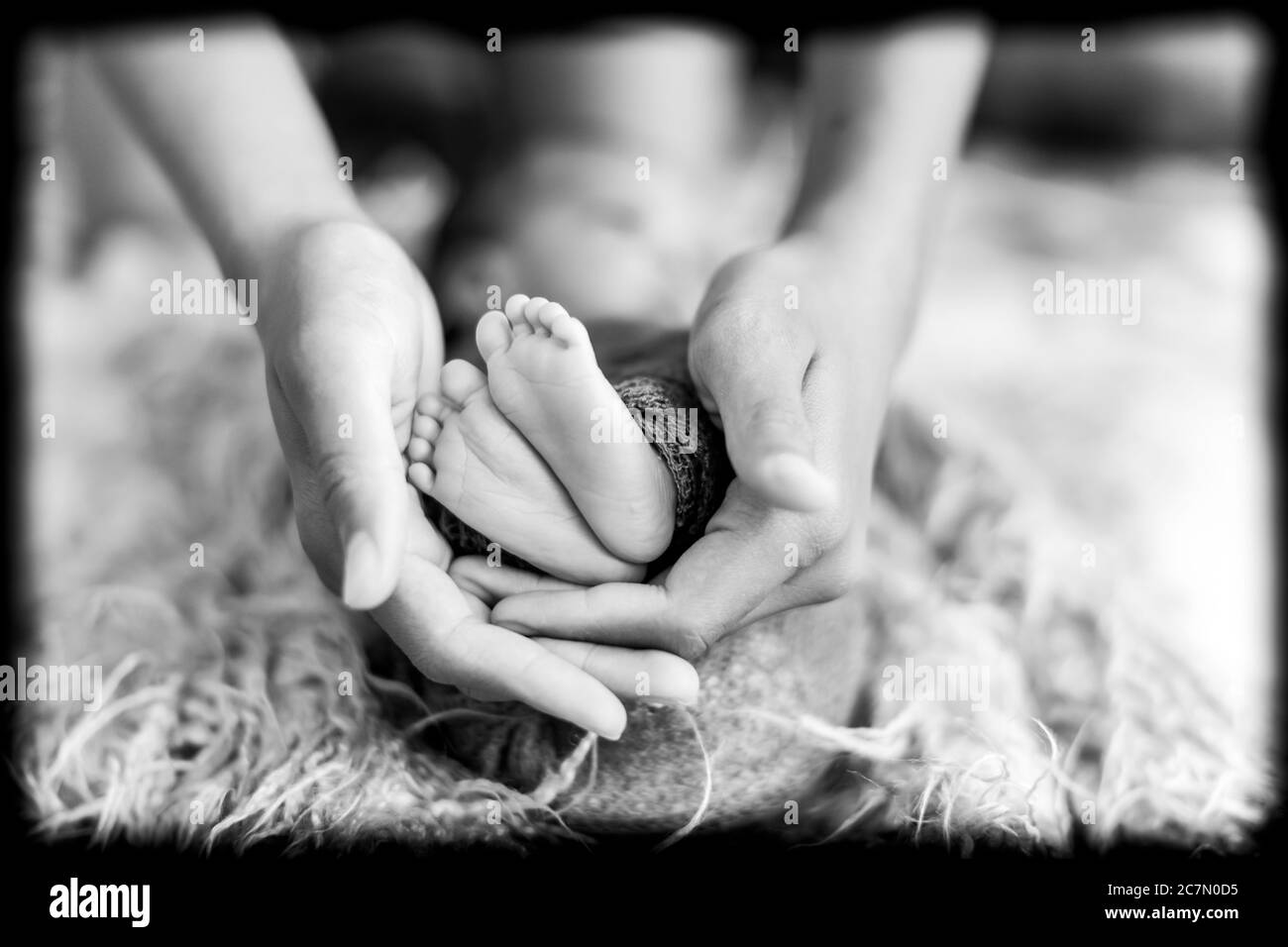 Immagine in bianco e nero dei piedini del bambino appoggiati alle mani Foto Stock