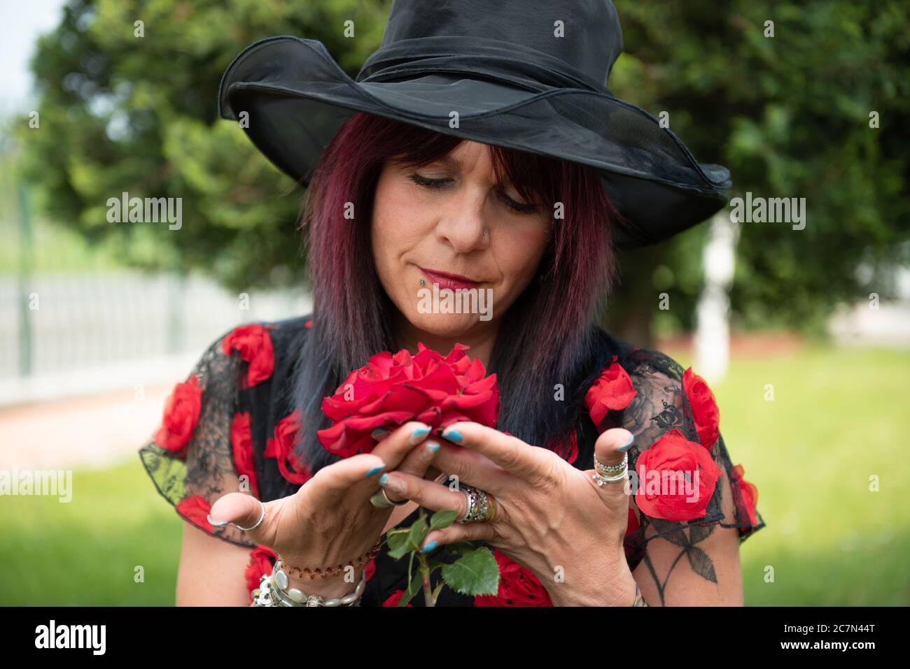 Donna sniffa l'aroma di bellissimi cespugli di rose rosse in un giardino botanico. Foto Stock