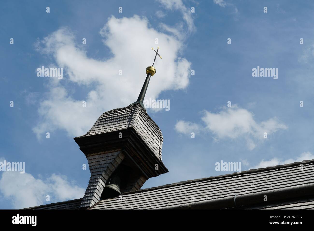 Un vecchio campanile su una chiesa del villaggio con una croce sulla cima. Il campanile e il tetto sono coperti da tegole di legno. Foto Stock