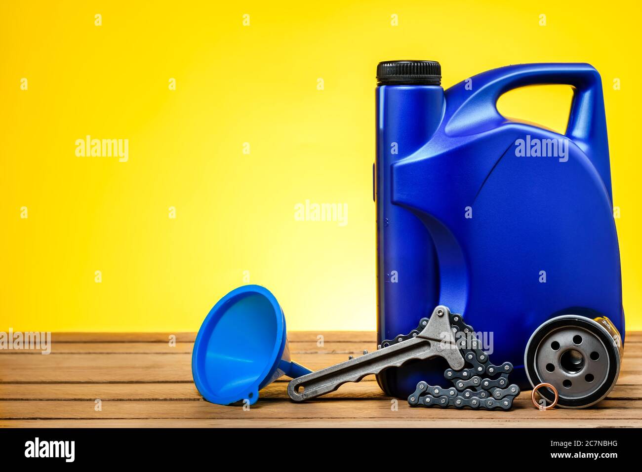 Filtro olio per auto, lattina in plastica per oli motore e chiave per filtro olio su un tavolo di legno davanti a uno sfondo giallo con spazio libero per il testo Foto Stock