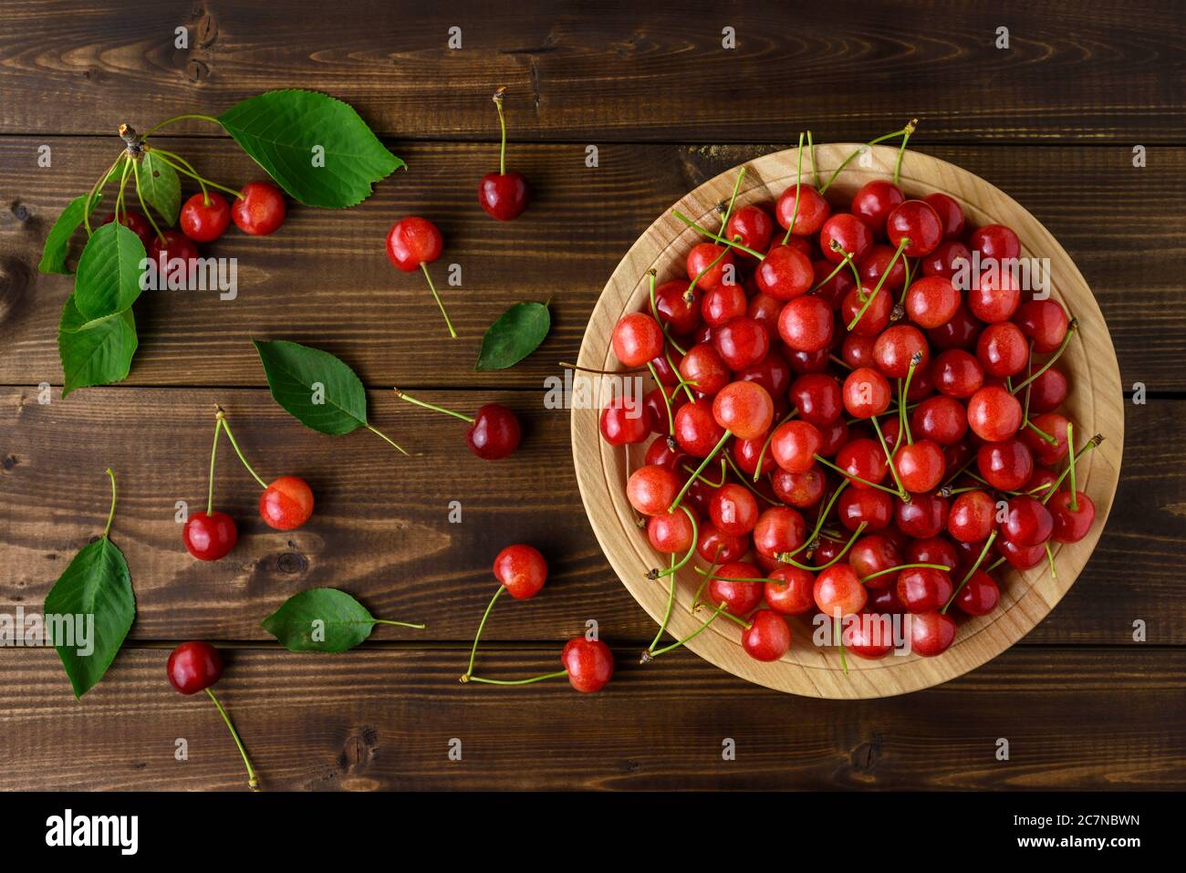 Ciliegie rosse dolci in un piatto di legno e foglie verdi su un tavolo di legno marrone. Vista dall'alto. Foto Stock