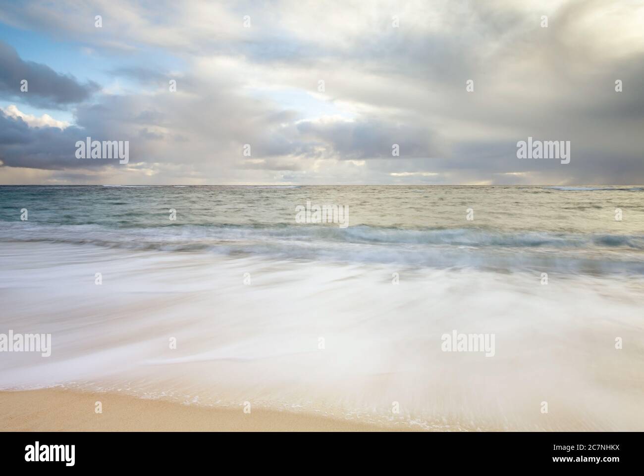 Onde che si infrangono sulla sabbia in spiaggia su un giorno nuvoloso Foto Stock