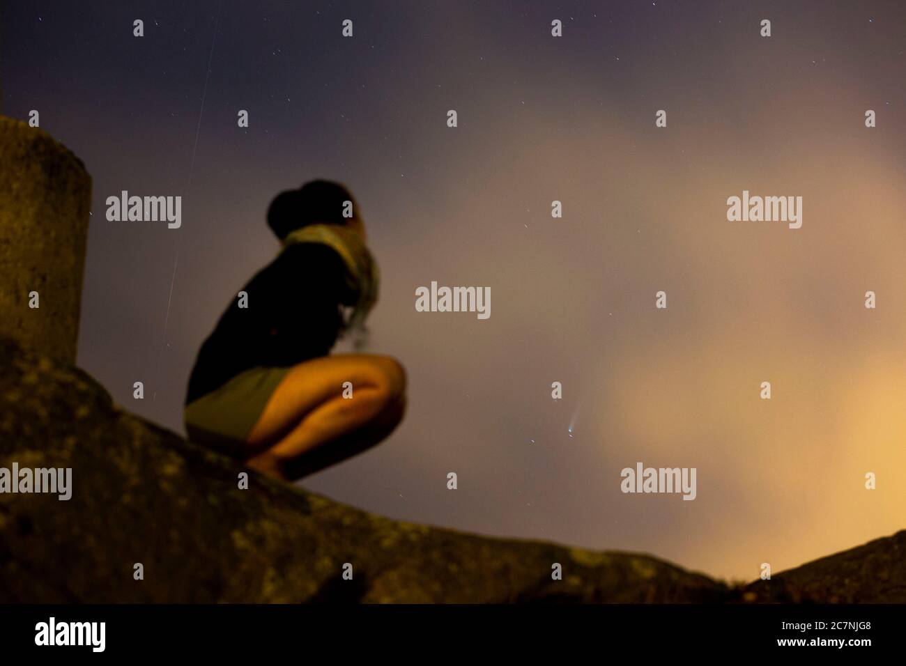 Una ragazza è vista guardare la Comet NEOWISE o C/2020 F3 dopo il tramonto con nuvole di fumo a causa dei forti incendi intorno alla città di Porto, Portogallo. Il 18 luglio 2020. - sul retro della ragazza anche aar una stella di tiro lasciando la sua traccia os l'immagine. Foto Stock