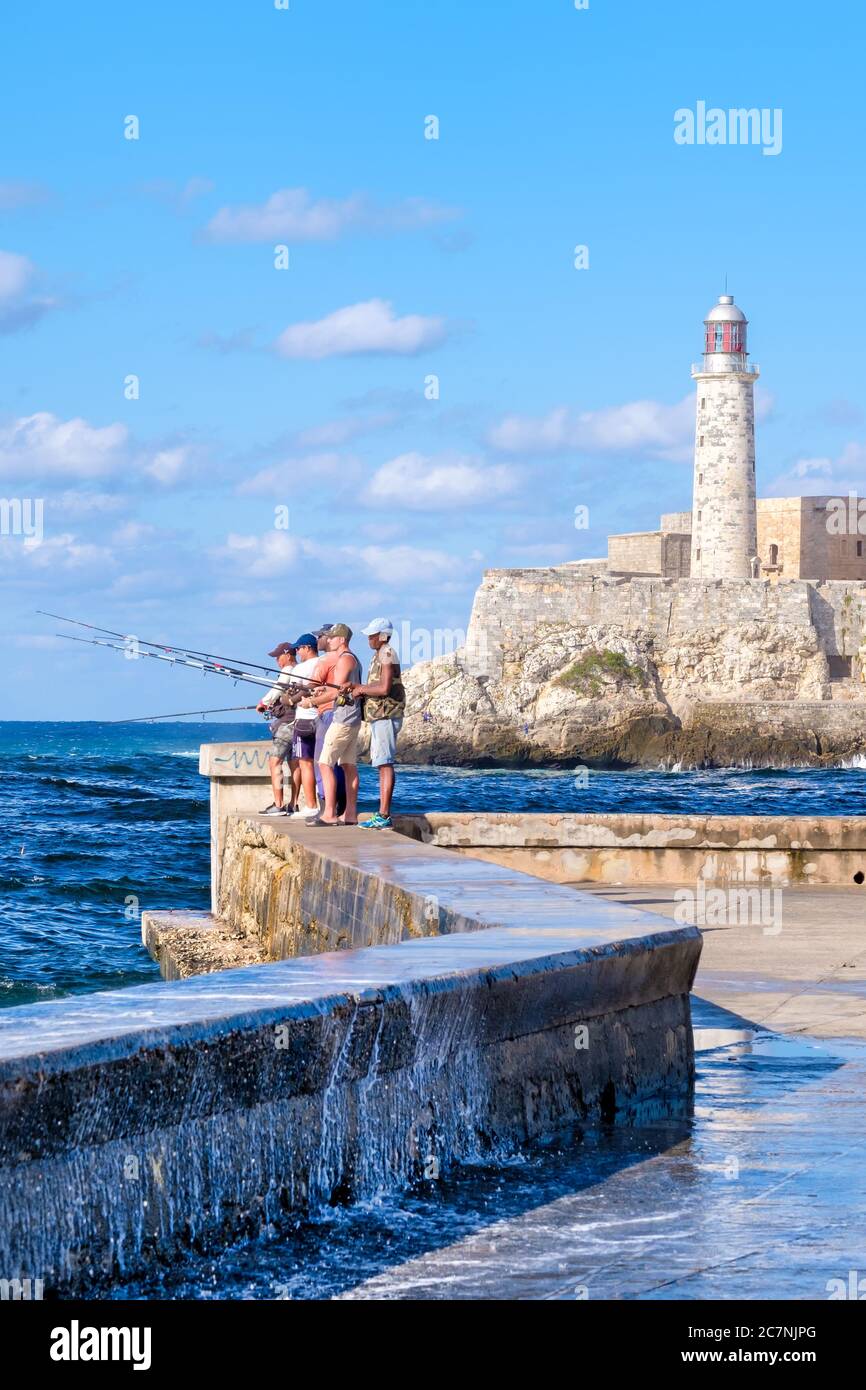 La gente pesca al muro di malecon a l'Avana con la fortezza di El Morro sullo sfondo Foto Stock