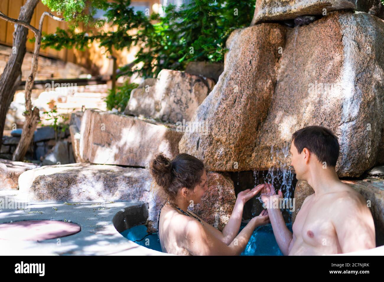 Giovane donna uomo romantica coppia rilassante nuoto in freddo tuffo pietra cascata in giapponese spa piscina con colorata acqua blu in Giappone onsen Foto Stock