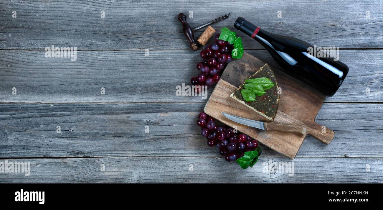 Cuneo di formaggio fresco con una bottiglia di vino rosso più foglie di basilico e uva su legno rustico con spazio copia disponibile Foto Stock