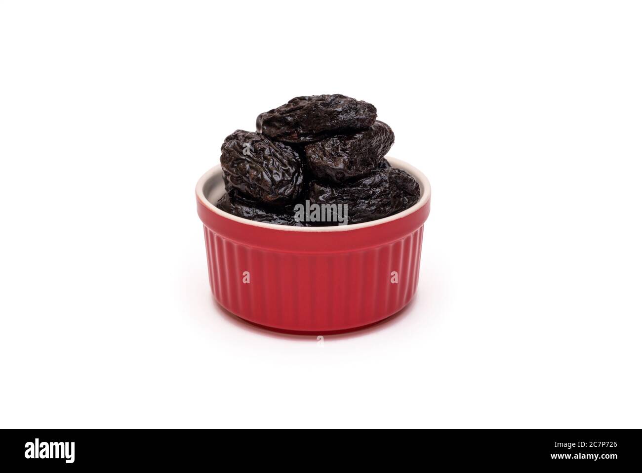 Prugne o prugne secche in ciotola rossa in ceramica su sfondo bianco. Concetto naturale di dolci sani. Primo piano. Spazio di copia Foto Stock