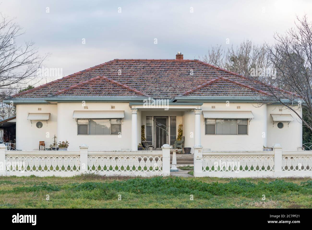 Una casa australiana post-guerra in doppio mattone e cotto con tetto in cotto con un esterno in cemento dipinto e finestre a oblò in stile P&o che si affacciano verso l'esterno Foto Stock