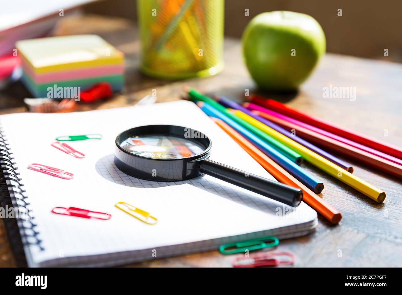 Torna a scuola: Nota libro, matite, loupa, mela verde su tavolo di legno Foto Stock