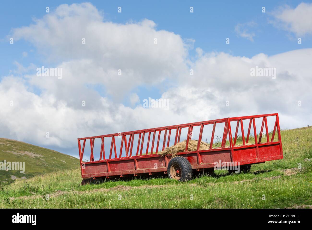 Un carro da fieno di fattoria dipinto di rosso su una collina nel periodo estivo Foto Stock
