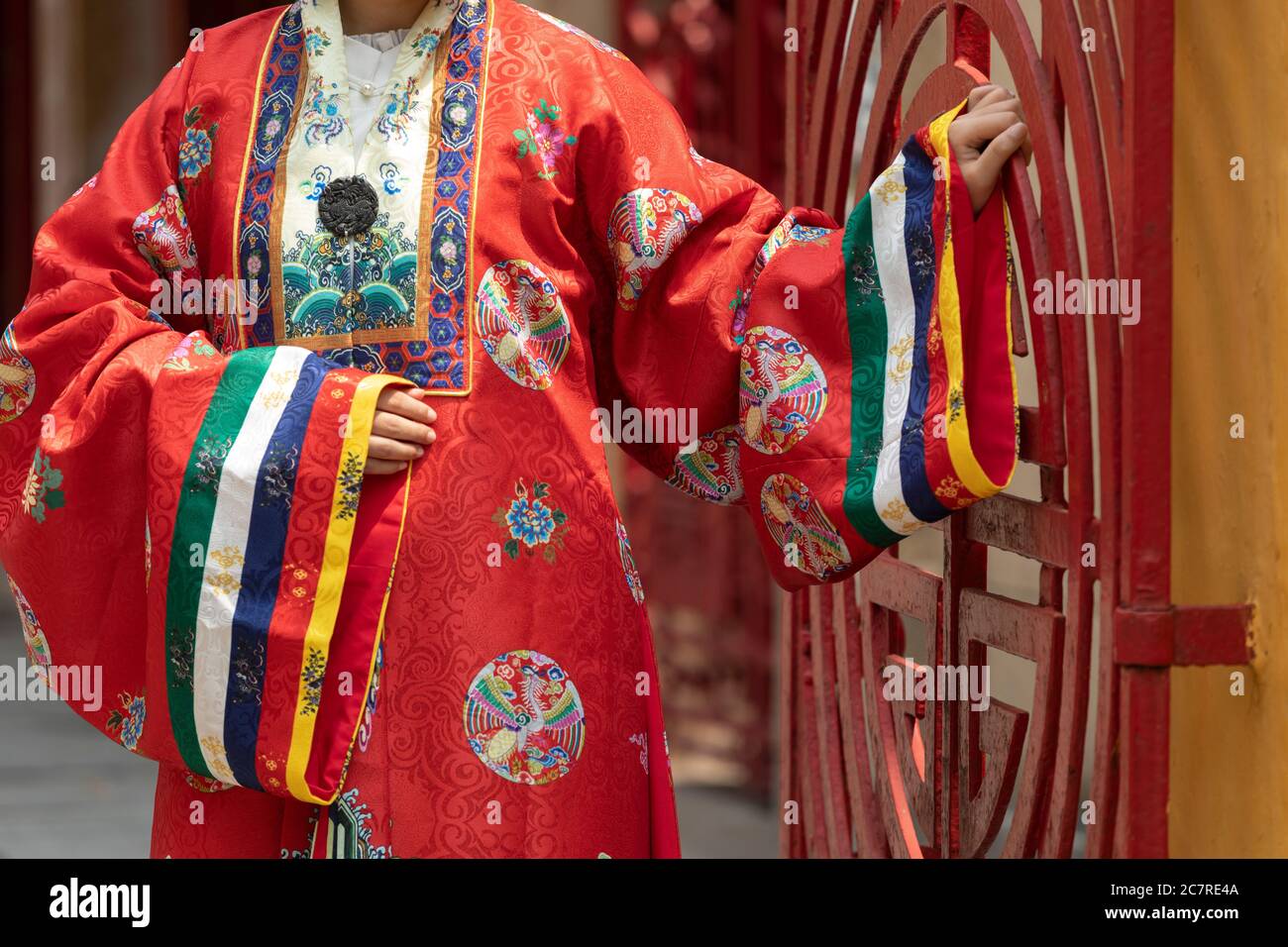 Dettaglio di tradizionali accappatoi di seta rossa vietnamita. Il modello è in piedi accanto a un cancello rosso. Questi accappatoi sono stati indossati da re Foto Stock
