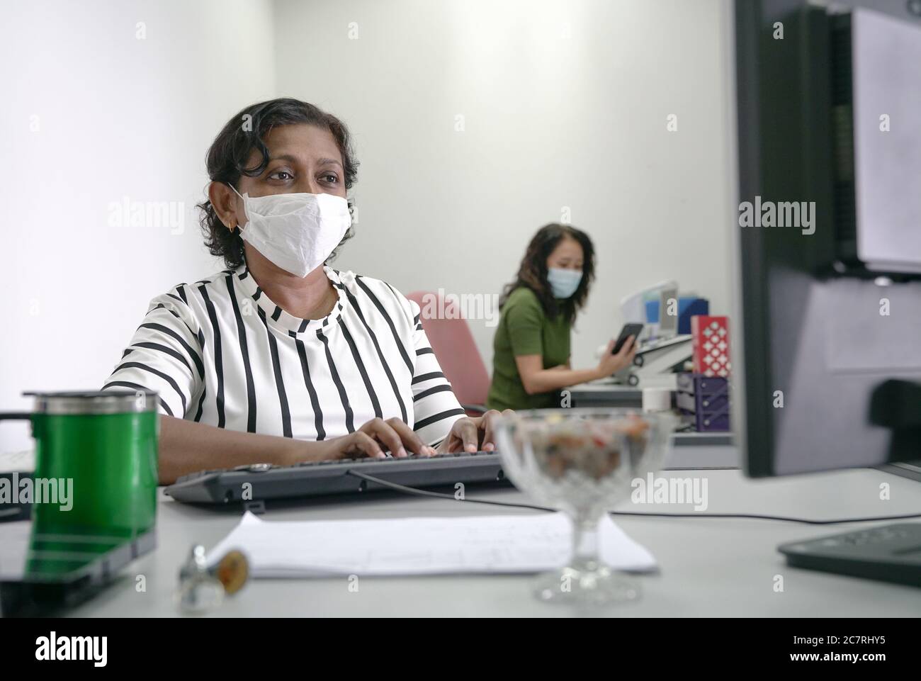 Dipendenti o donne d'affari con maschere di protezione per tornare al lavoro in ufficio dopo il blocco. Foto Stock