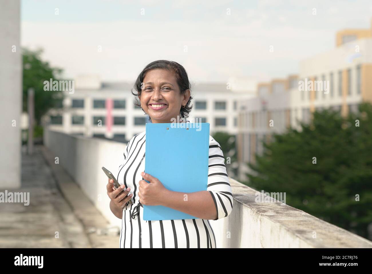 Ritratto di una bella donna d'affari indiana sorridente. Esterno con edifici per uffici sullo sfondo. Foto Stock