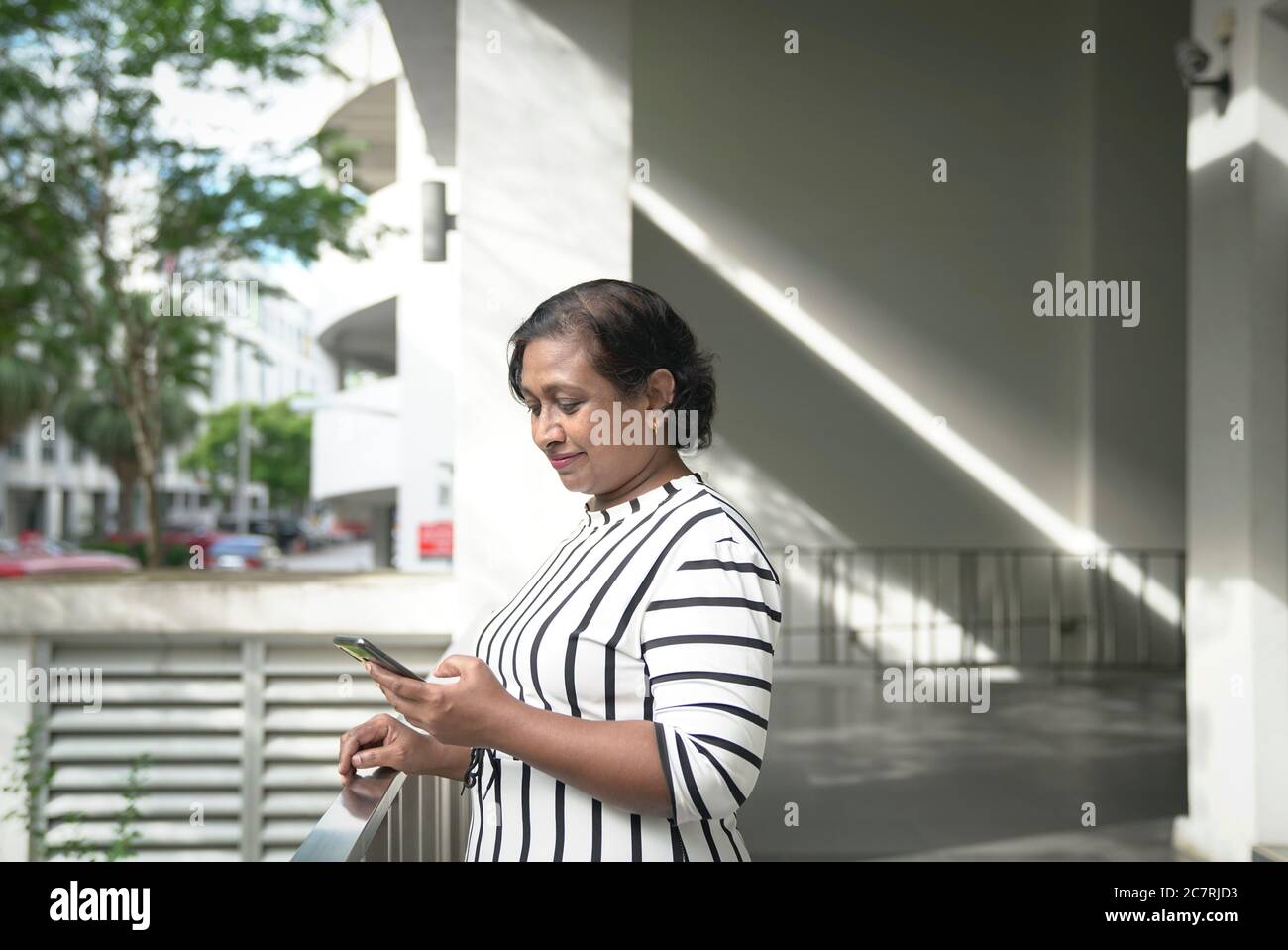 Donna indiana di affari che legge il suo cellulare nel corridoio dell'ufficio. Porta d'ingresso e sfondo urbano. Foto Stock
