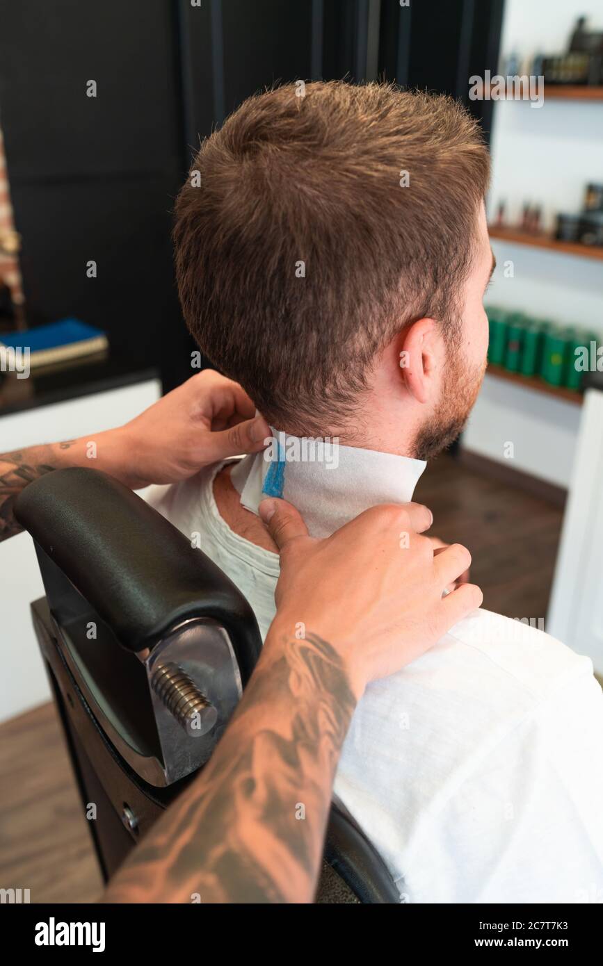 Parrucchiere con tatuaggi che mettono una striscia di collo intorno al cliente  collo sotto le luci Foto stock - Alamy