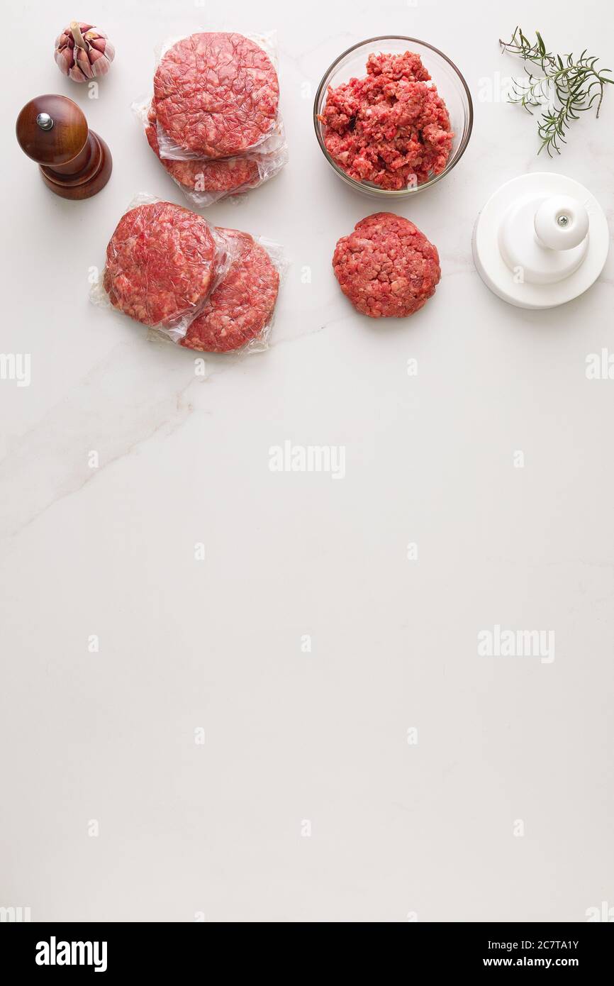 Vista dall'alto degli ingredienti per preparare un hamburger. In un tavolo di marmo, una ciotola di vetro con carne, pepe di legno, aglio, modellatore di hamburger, macinacaffè e rosem Foto Stock