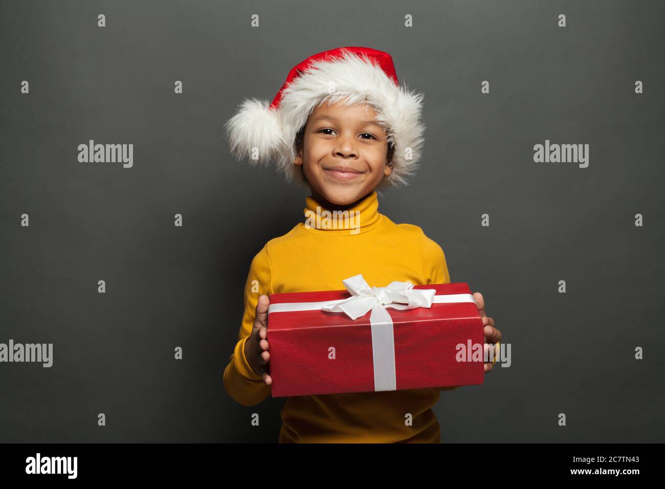 Babbo Natale nero con scatola Natale rossa con nastro bianco setoso su sfondo grigio Foto Stock